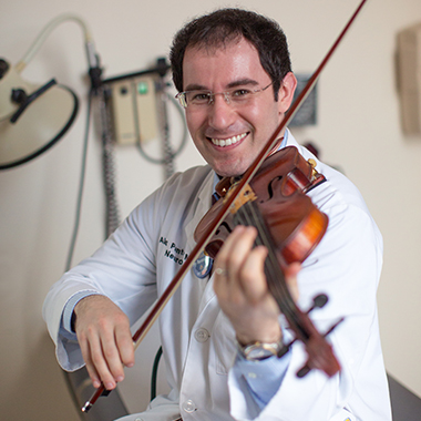 Alexander Pantelyat, wearing a white lab coat, plays violin in a patient examination room